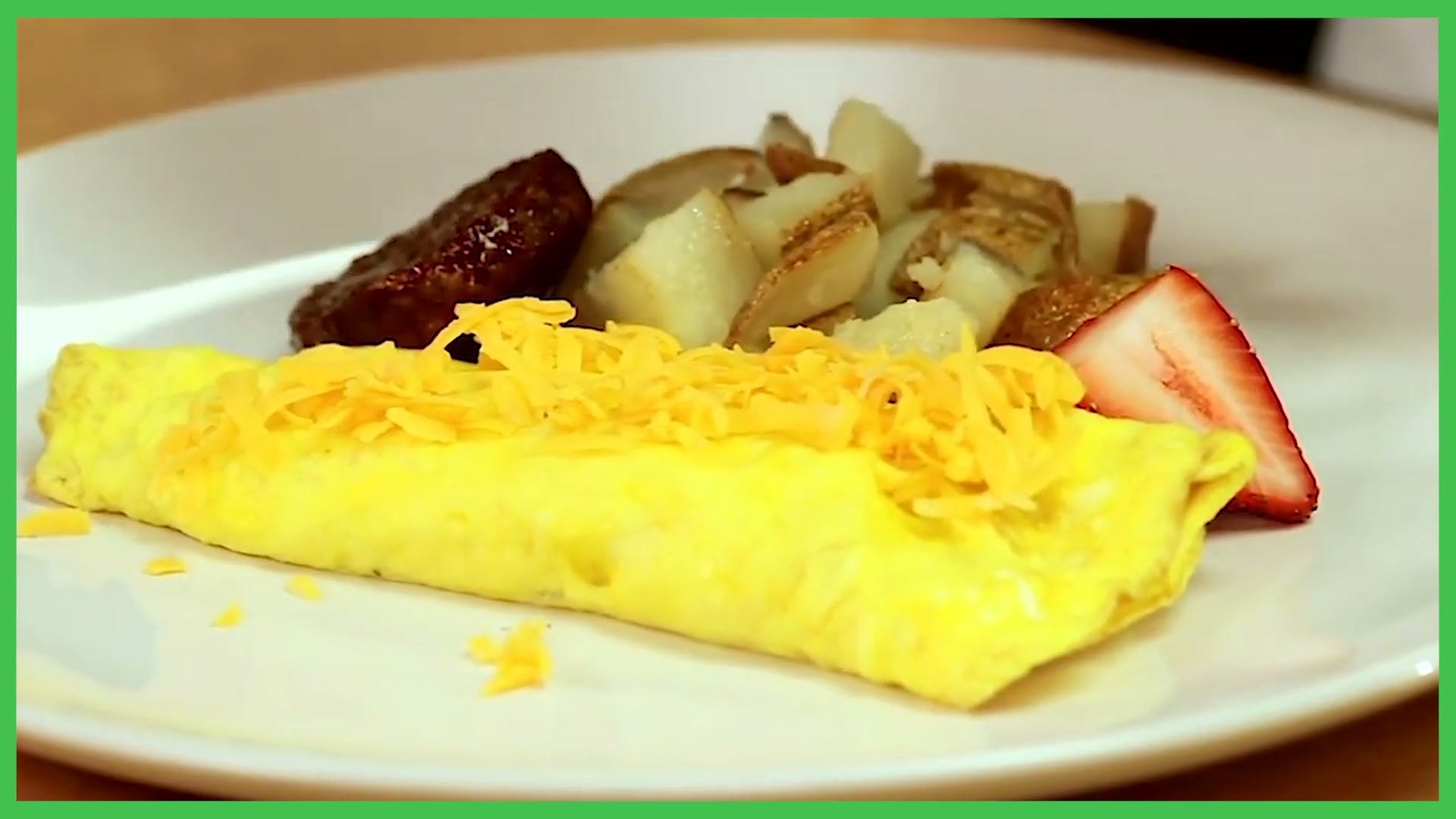 A folded omelette on a white plate with breakfast potatoes, sausage, and a fanned strawberry